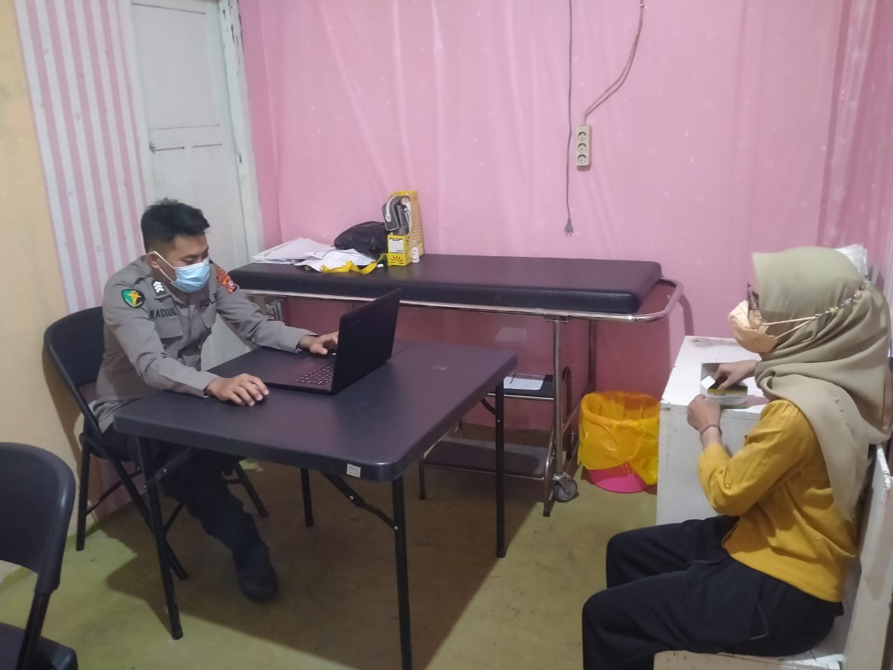Brigpol La Ode Nasrul Pangeran sedang sibuk mengecek laptop yang menjadi sarana penginputan penerima vaksinasi Covid-19. Di depannya, ada bidan Sari Mawaddah yang sedang "menganggur" dari aktivitas vaksinasi lantaran stok habis. (Foto Texandi)